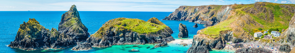 Serrated rocks extending out into the sea from a sandy cove, surrounded by a calm turquoise sea