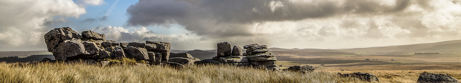 Low rocky tor in the foreground, with an expansive view across rough moorland beyond