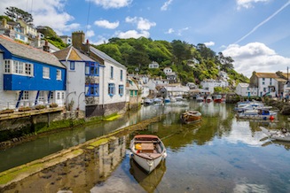 Boats inn Polperro harbour with white-washed cottages and a wooded hillside in the background