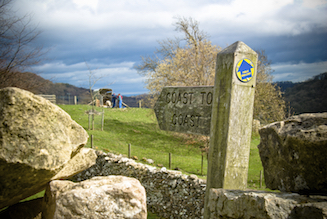 Wooden finger post pointing the route of the Coast to Coast over a stone stile