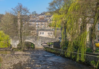 Stone bridge over the River at Hebden Bridge, with old mill buildings and millworkers cottages in the background